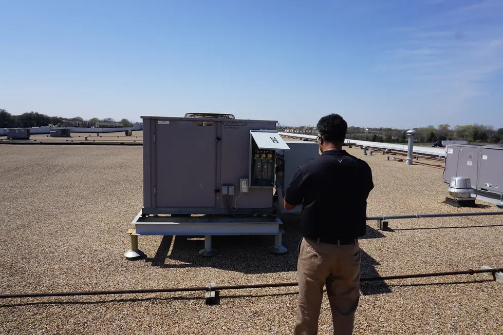 Inspector at an open rooftop package unit on a gravel ballasted commercial roof in Dallas